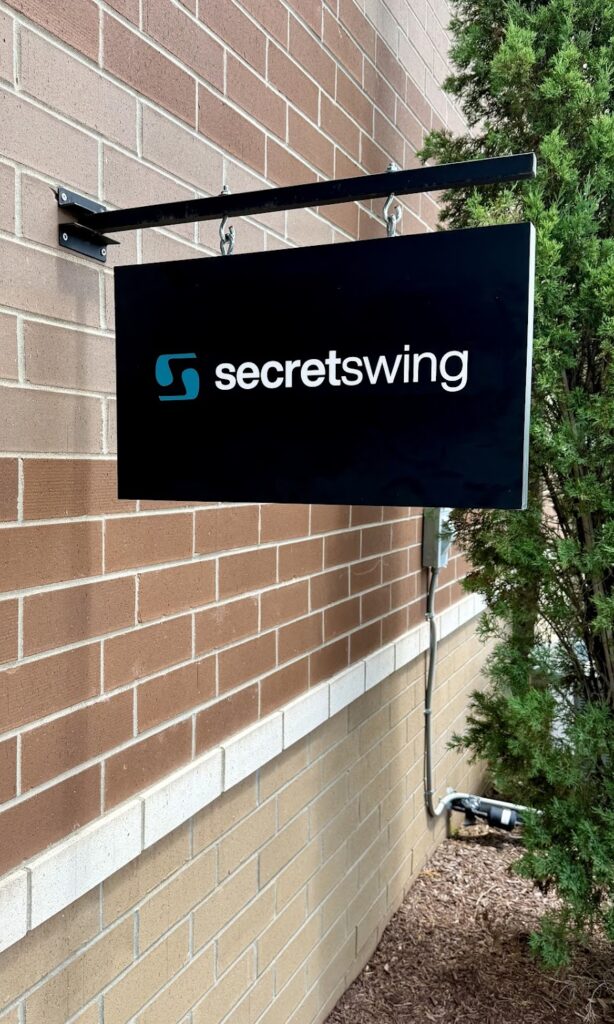 The Secret Swing entry sign — black hanging sign with the brand logo at the rear of 879 Greenlea Blvd Suite 105B, Gallatin TN